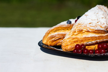 Delicious breakfast with fresh croissants and ripe berries and mint tea on the background of green grass. Summer breakfast time.