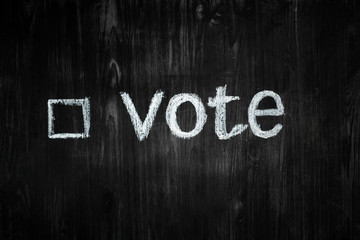Political activism sign: handwritten word "vote" in black background. Election process concept: word vote and an empty tick box in wood low-key background