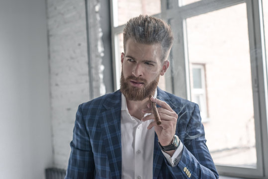 A portrait of a handsome mature man in a formal suit smoking a cigar in the interior. Men's beauty, fashion.