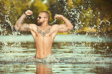 Muscle tattooed man execising in summe city lake water