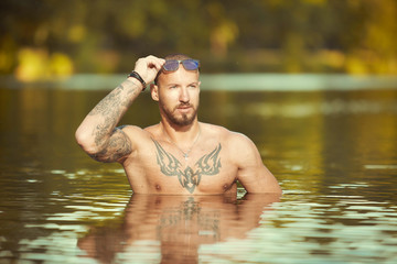 Muscle tattooed man execising in summe city lake water