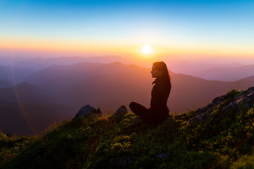 Woman sitting on a rock over mountains at sunset. Girl on the background of mountain peaks. Woman hiking in mountains