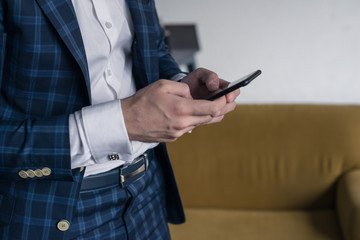 close-up of a man who holds in his hand a smartphone . He is standing im loft interior . business person browsing internet or connecting to wireless via touchscreen pad