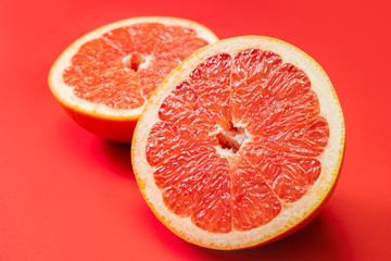 Grapefruit cut in half on vivid red background. Fruitarianism, vegetarian or vegan food: close-up view of fresh and ripe citrus fruit in bright colors