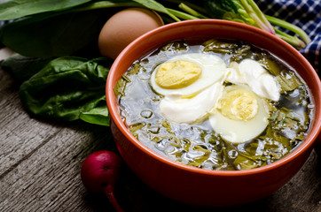 Green borscht with sorrel, spinach and potato, topped with boiled egg and sour cream on a vintage wooden table.
