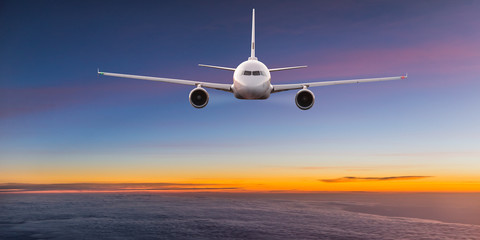 Fototapeta premium Komercyjny samolot odrzutowy lecący nad dramatycznymi chmurami w pięknym świetle zachodzącego słońca. Koncepcja podróży.
