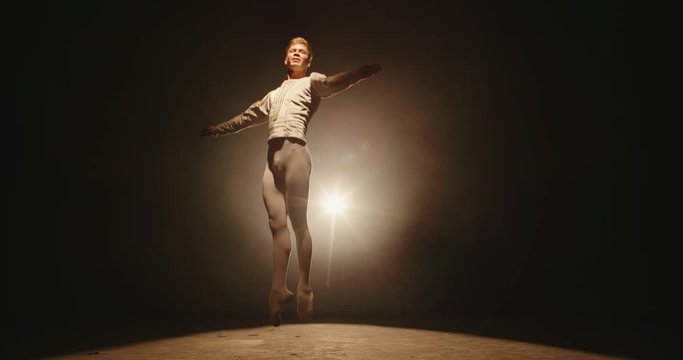 Caucasian male ballet dancer performing on stage, spotted by white light. Young choreographer showing creative performance, isolated on black background 4k footage
