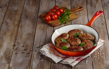 Fried meat cutlets on a red cast-iron pan on a wooden background. Copy space