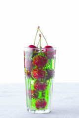 Cherry cocktail. Red cherries in a glass on a white background. Green carbonated drink with sweet cherries. Copy space