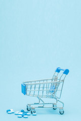 Pills and Shopping trolley on blue background. Creative idea for health care cost, drugstore, health insurance and pharmaceutical company business concept. Copy space