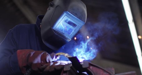 4K Welder working in metal workshop & lifting up visor to check his work