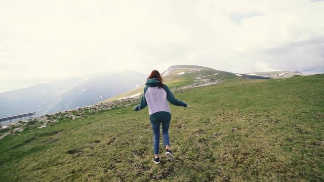 A young woman hiker running and spinning on top of a mountain. Transalpina, Carpathian mountains in Romania slow motion