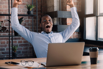 He is a winner! Young african american office worker or businessman throwing hands in air in...
