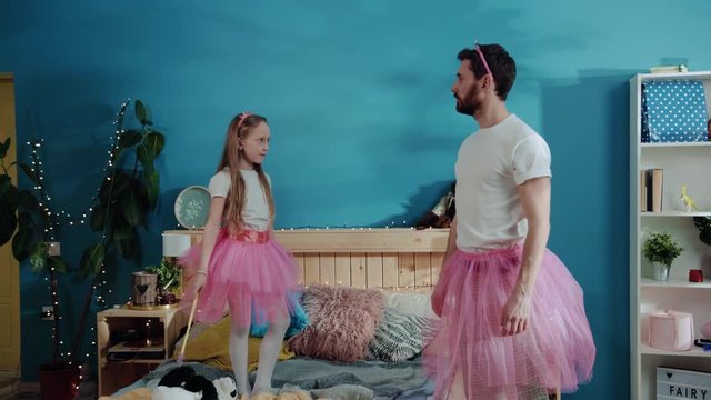 Lovely pretty young daddy and his daughter dressed as fairies playing at magic party together. Cute girl little princess standing like ballerina and her father repeating her pose in wrong way. Funny