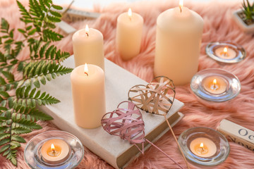 Beautiful burning candles with book on furry plaid