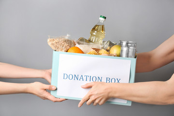 Volunteer giving box with donation food to poor woman against grey background
