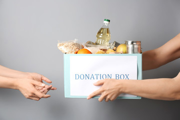 Volunteer giving box with donation food to poor woman against grey background