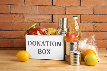 Box with donation food on table near brick wall