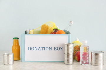Box with donation food on table against light background