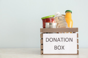 Box with donation food on table against light background