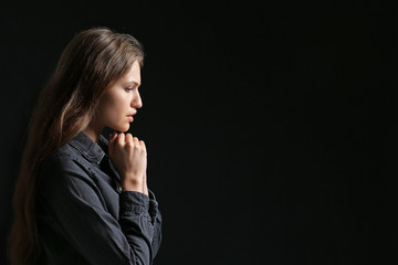 Religious young woman praying to God on dark background
