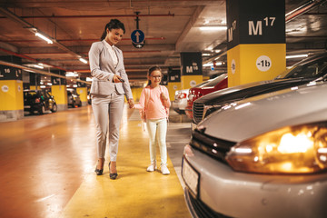 Young businesswoman with her daughter in a public underground garage. - obrazy, fototapety, plakaty