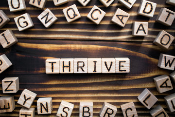 Obraz premium word thrive composed of wooden cubes with letters, to grow, develop, or be successful concept, scattered around the cubes random letters, top view on wooden background