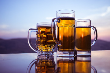 Glass of beer on a beach at sunset. Cooling summer drink concept. Close Up of A Glass of Draught Beer with the Bokeh of Sunlight Background