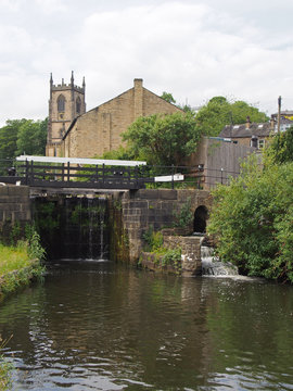 lock gates on the canal in sowerby bridge in west yorkshire with the historic christ church building surrounded by trees