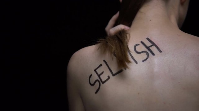 Trembling naked woman showing word selfish on shoulder, public opinion, problem