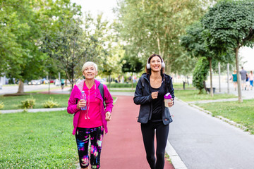 Happy mother and daughter jogging together outdoors in park.