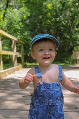 Happy smiling toddler boy in overalls in the park on bridge