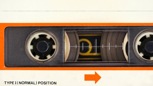 Close up of music cassette tape with blank white index label in use playing back in a deck player. Cassette tapes are most popular analogue audio format ever created with over 30 billion produced to d