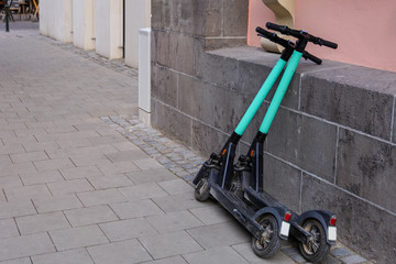 Two parking E-scooters , Eco friendly mobility concept of sharing transportation with Electric Scooter, lean against wall on sidewalk in old town Düsseldorf, Germany.