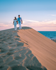 Maspalomas ,couple walking at the beach of Maspalomas Gran Canaria Spain, men and woman at the sand dunes desert of Maspalomas during a morning walk at sunrise - obrazy, fototapety, plakaty