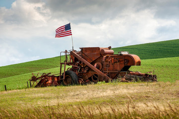 Fourth of July Patriotism On An old Harvester. An American flag flies over an abandoned wheat...