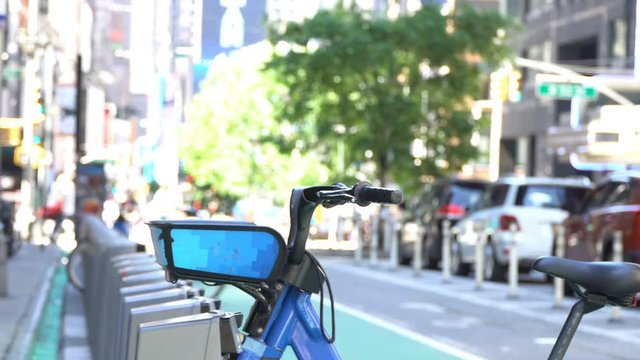 Bicycle rental station on a New York City avenue, defocused background shows an unrecognizable rider returning his bike