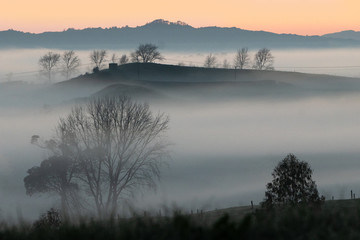 A magical looking sunrise with mist in the valleys and silhouettes of hills and trees. 