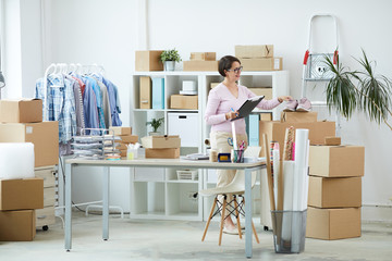 Young manager of online shop taking pair of pink footwear while going to pack them
