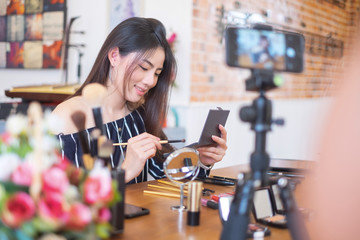 Happy girl blogger at cafe talking about makeup and beauty and recording video tutorial for...