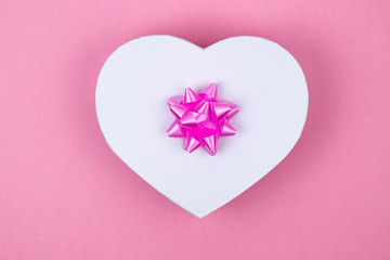 Heart shaped gift box with pink bow on a pink background. Mock up. Postcard for the holiday. Empty place for an inscription. 