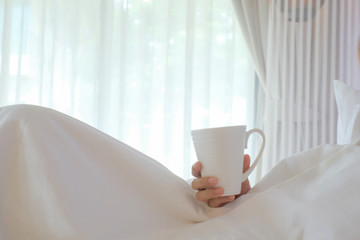 Asia woman holding coffee on white bed, morning concept.