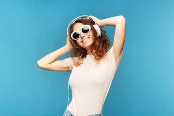 Young carefree brunette woman in jeans and t-shirt listening to music in headphones while enjoying...