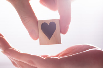 Male Hand Giving Wooden Block With Heart Shape To Female