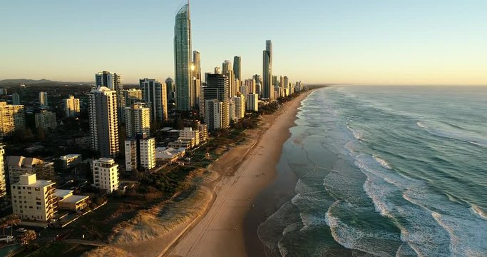 Long forward flying along waterfront of Surfers paradise high-rise towers above sandy beach and waves of Pacific ocean.