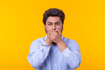 Indian man keep his mouth closed by his hands on yellow background. Secret, silence and no freedom...