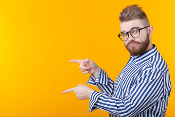 Solution is here. Handsome funny young man pointing copy space and looking at camera while standing against yellow background