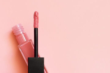 Liquid lipstick and applicator on coral pink color background. Open tube of lip gloss and wand brush with makeup product on pastel coral surface. Top view, flat lay, copy space - obrazy, fototapety, plakaty