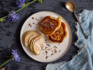 Breakfast with fritters and pears with sweet syrup on a dark background with a few sprigs of blossoming chicory and a teaspoon