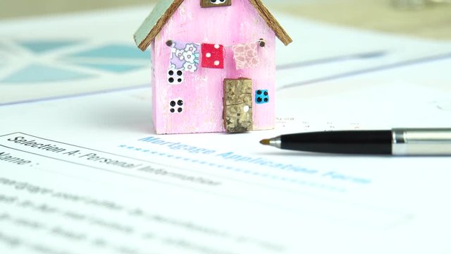 Mortgage loan and real estate property concept : Mortgage application form with pink model wood house, pen on purchasers document for signature contact. Idea for refinance agreement for raise funds.